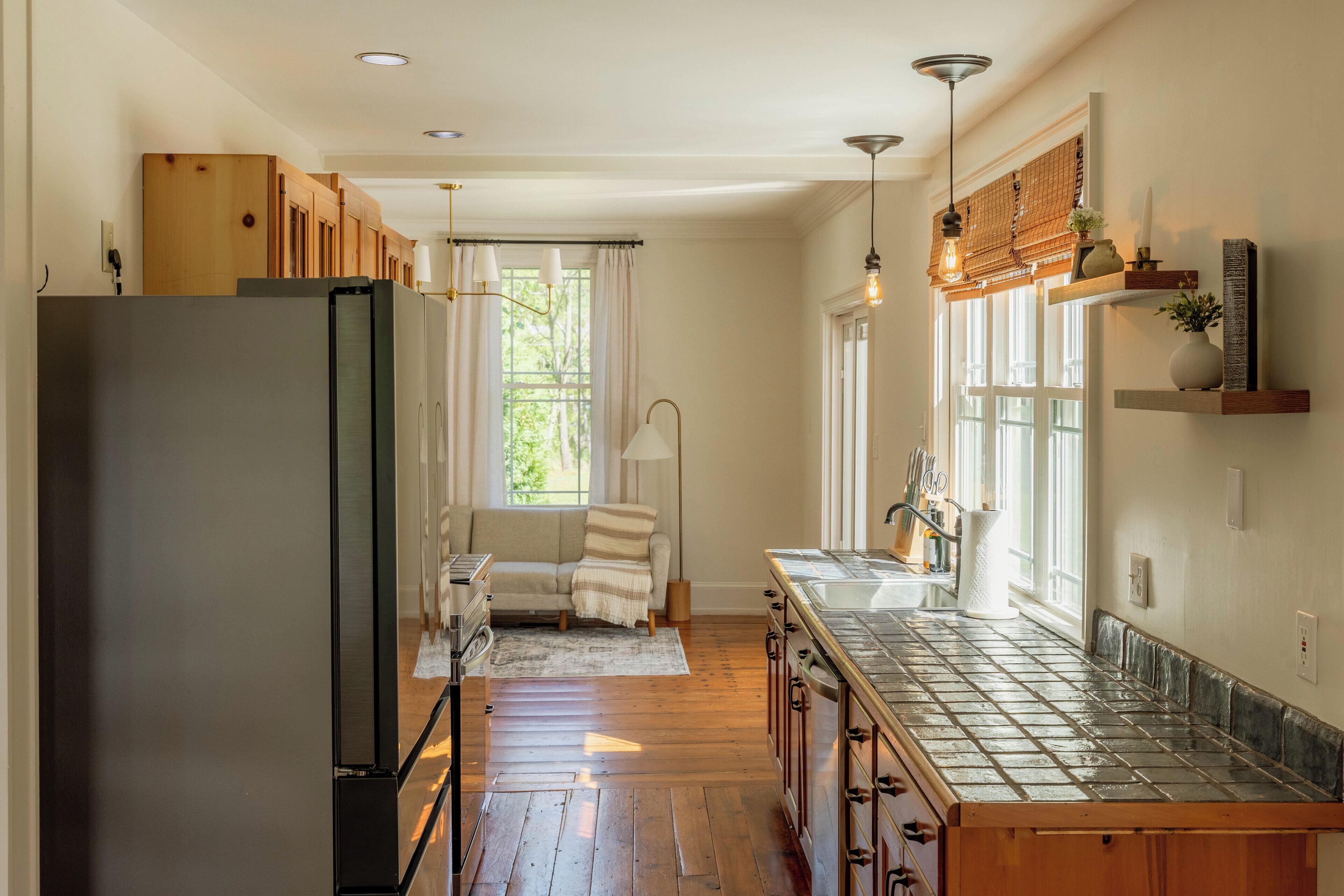 A kitchen with wooden cabinets, a refrigerator, a sink, and a window with curtains.
