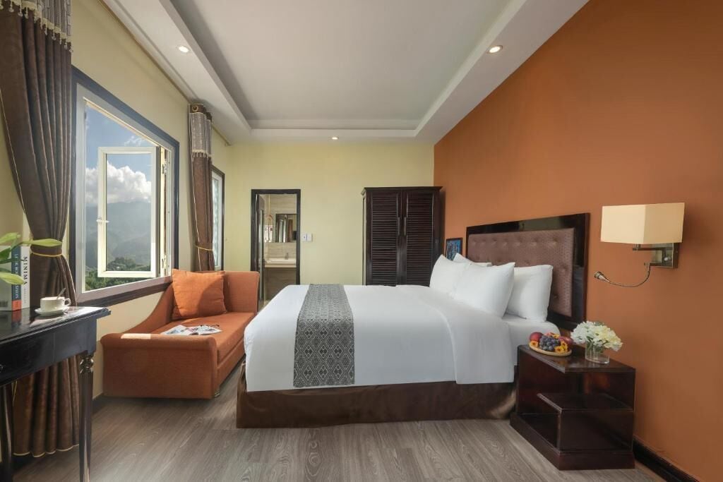 Habitación de hotel con una cama grande, un sofá, un escritorio y una ventana con cortinas.