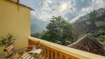 A balcony with a view of a bridge and mountains, a table with a bowl of fruit, and a potted plant.