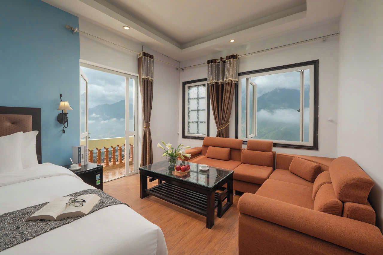 A hotel room with a bed, a sofa, a coffee table, and a view of mountains through large windows.