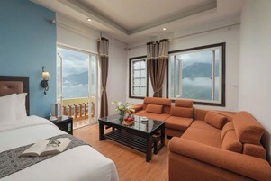 A hotel room with a bed, a sofa, a coffee table, and a view of mountains through large windows.