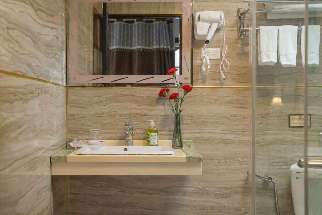 A bathroom with a marble sink, a mirror, a hairdryer, and a glass shower enclosure.