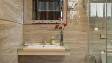 A bathroom with a marble sink, a mirror, a hairdryer, and a glass shower enclosure.