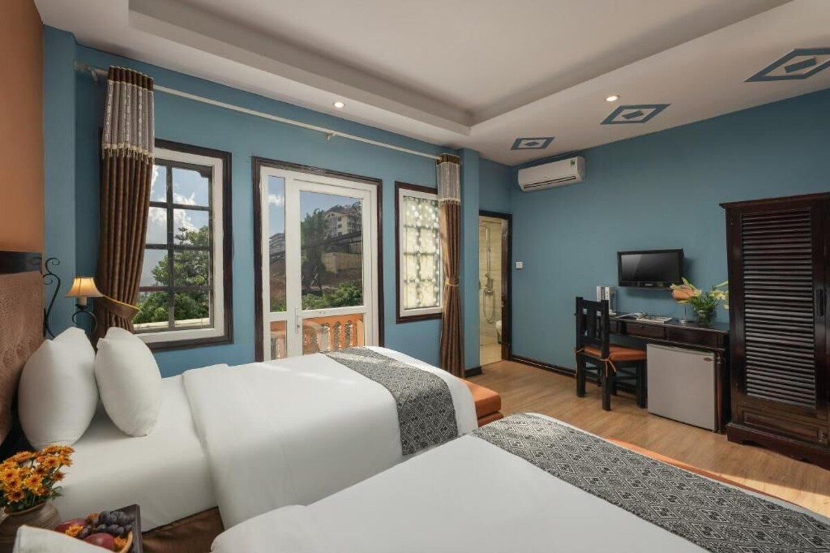 A hotel room with two beds, a desk, a television, and a view of the outdoors.