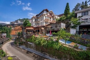 Un edificio de varios pisos con balcones, una calle al frente y un pequeño jardín.