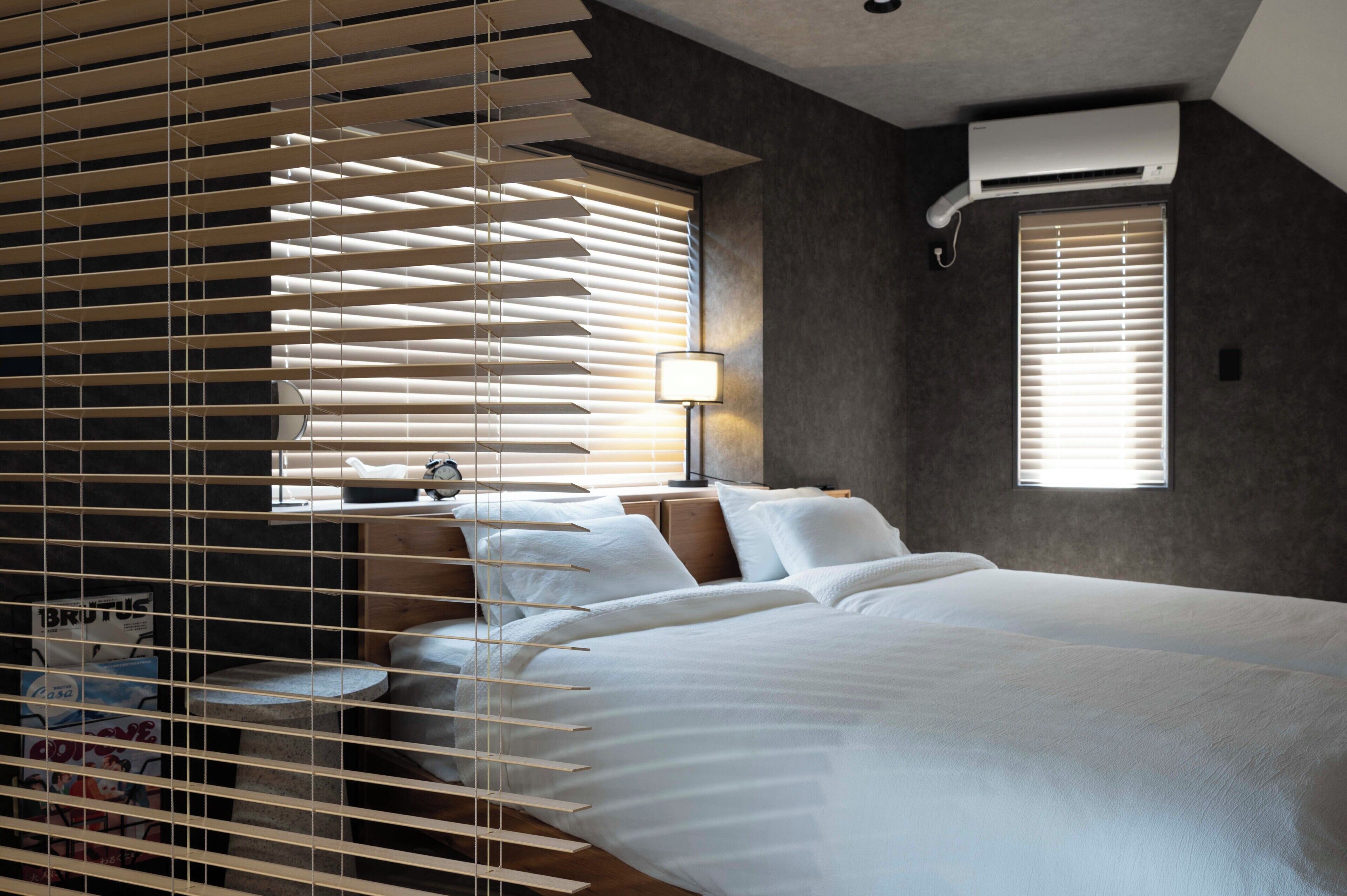 Un dormitorio moderno con una cama grande, una mesita de noche, una lámpara y una ventana con persianas.