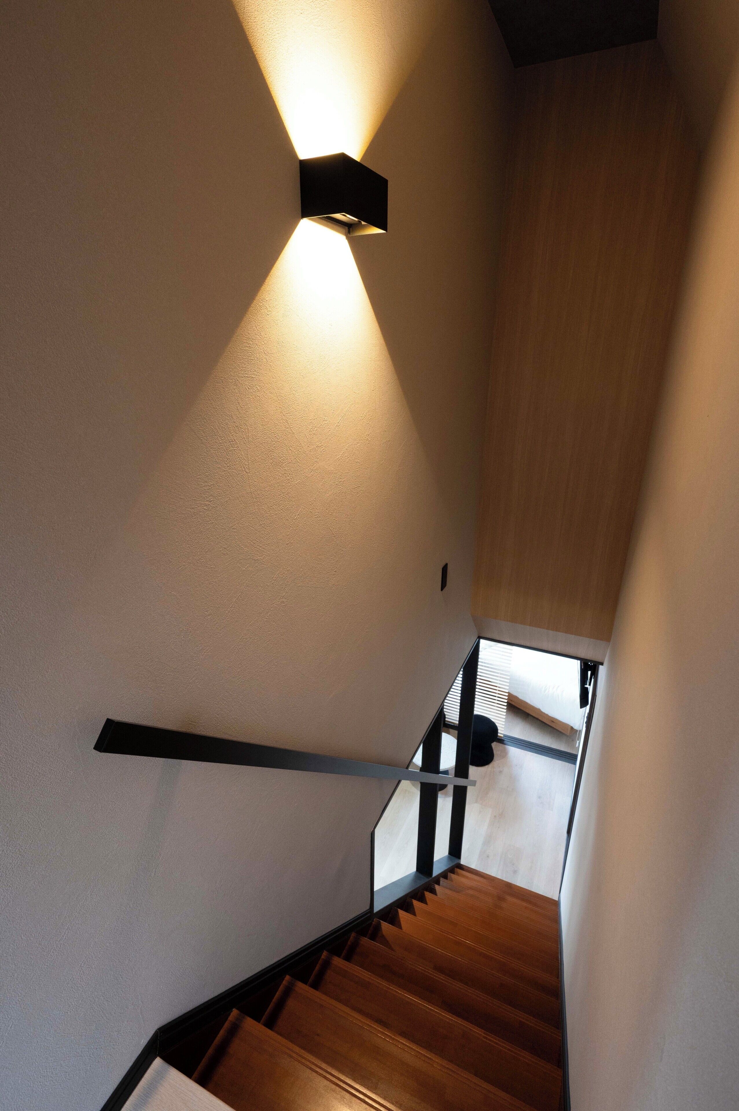 A staircase with wooden steps and a handrail, leading to a room with a bed and a window.