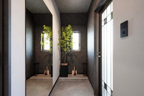 Un couloir avec une grande fenêtre, une plante en pot et une porte dotée d’un interrupteur.
