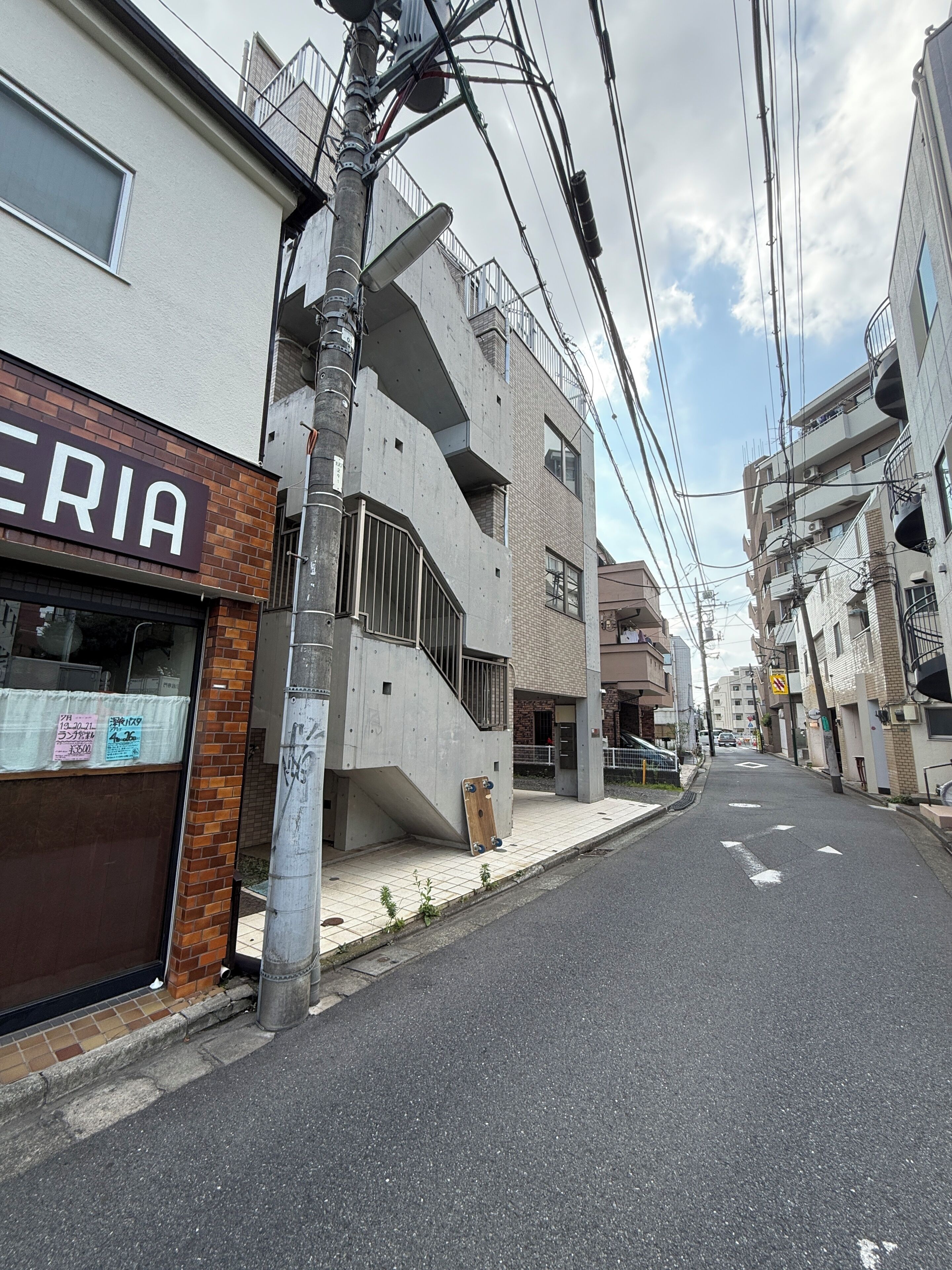 A narrow urban street with residential buildings, a visible storefront with a sign, and a concrete utility pole.