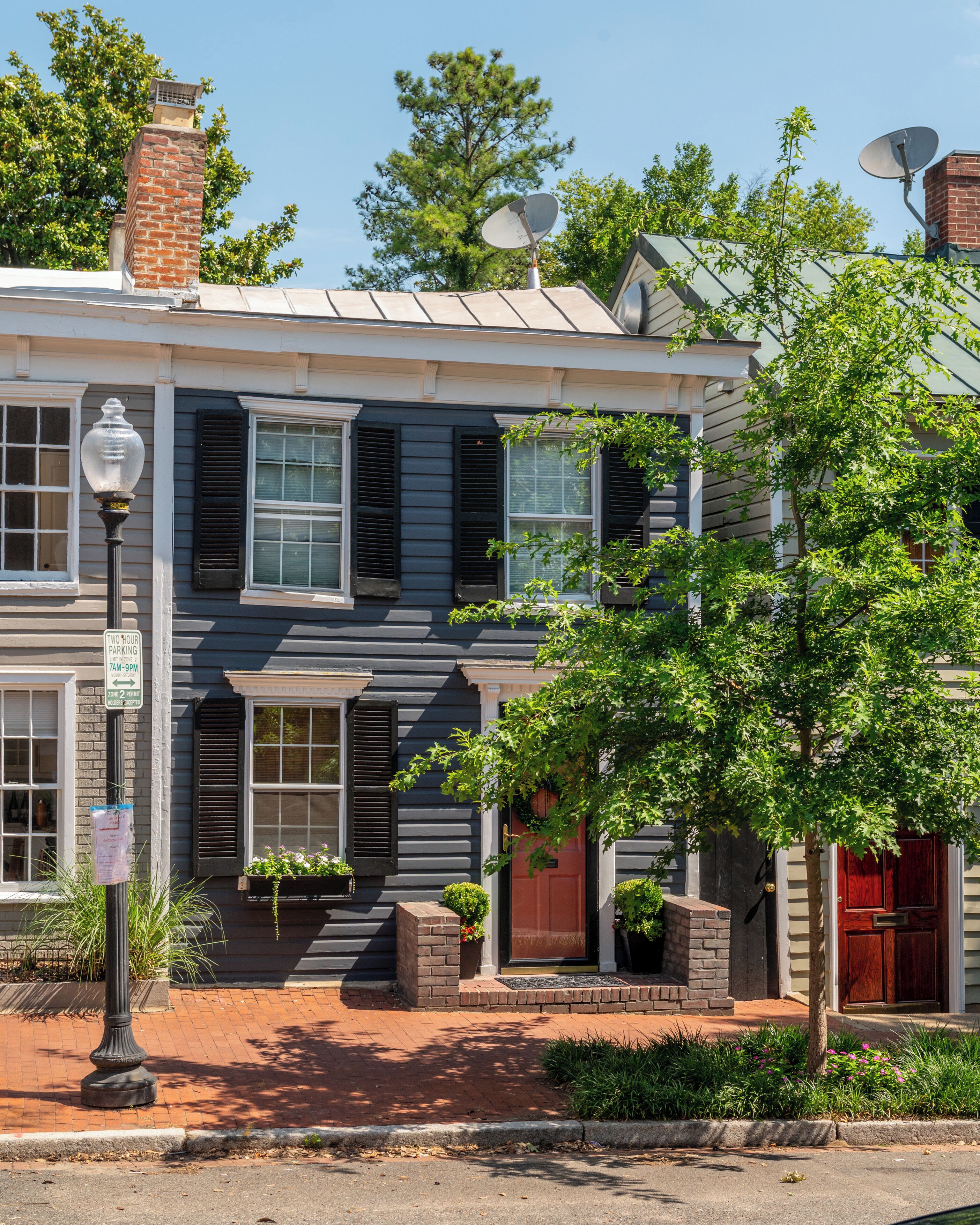 A two-story house with a brick chimney, satellite dishes, and a two-hour parking sign.