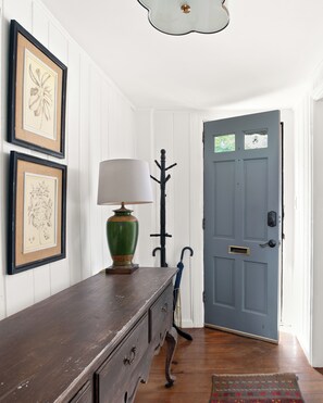 A hallway with a wooden dresser, framed botanical prints, a green lamp, a blue door, and a patterned rug. - Georgetown’s Secret Garden in the West Village, Steps from the University (Washington)
