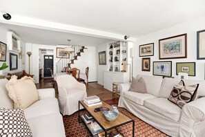 A spacious living room with a staircase leading to another level, a dining area with a table and chairs, and a wall adorned with framed artwork. - Georgetown’s Secret Garden in the West Village, Steps from the University (Washington)