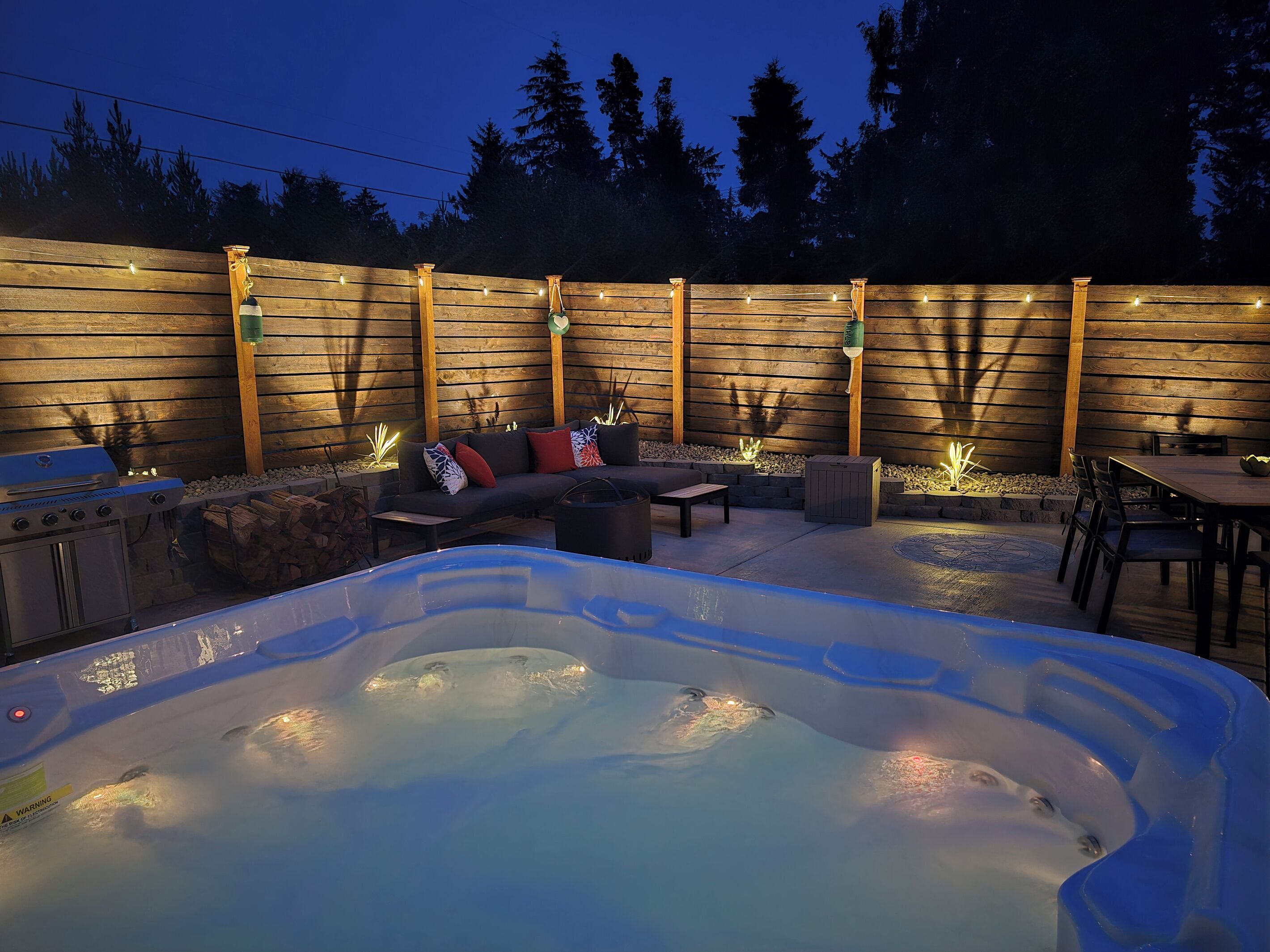 An outdoor patio with a hot tub, a barbecue grill, a sofa, and a dining table.