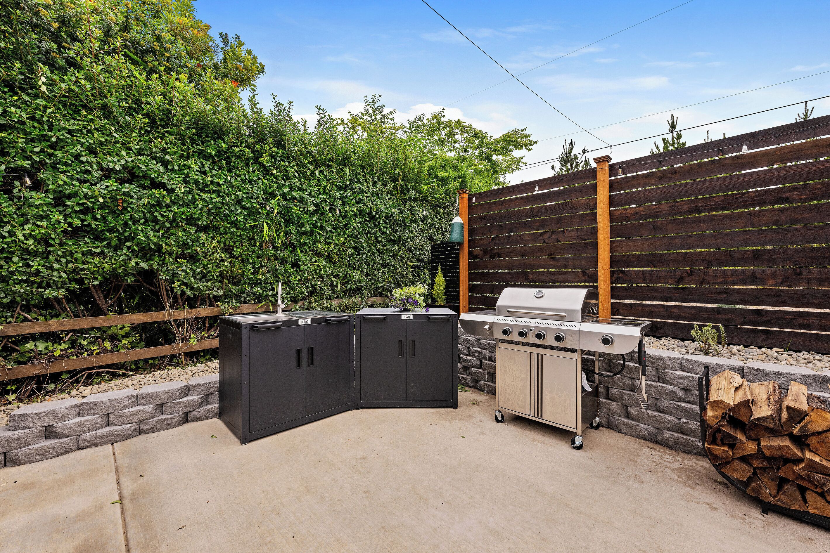 An outdoor barbecue area with a grill, storage cabinets, and a wooden fence.