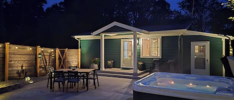 Un espace patio avec un jacuzzi, des sièges d’extérieur et une maison dotée d’un porche couvert.