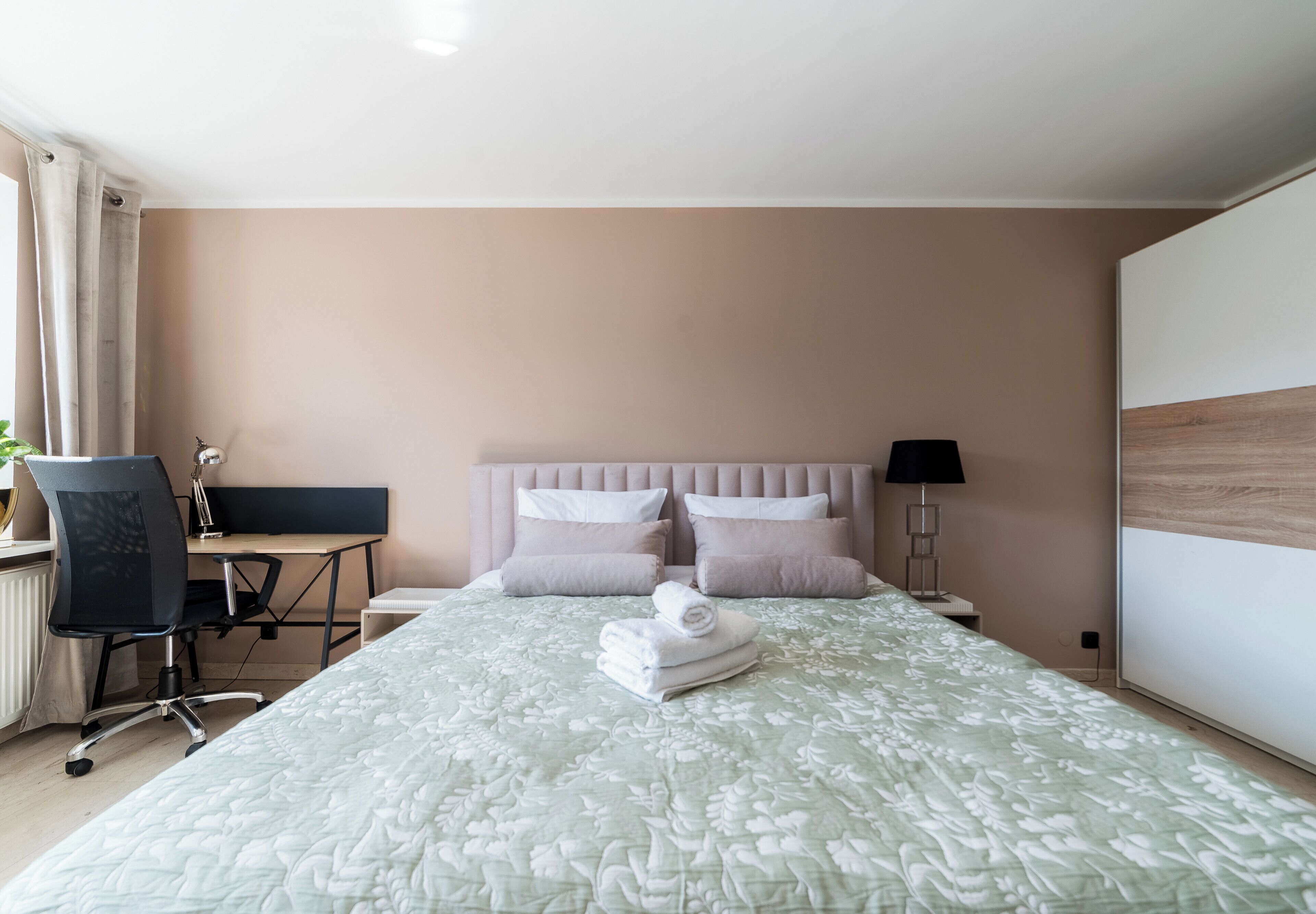A hotel room with a bed, a desk, a chair, and a lamp.