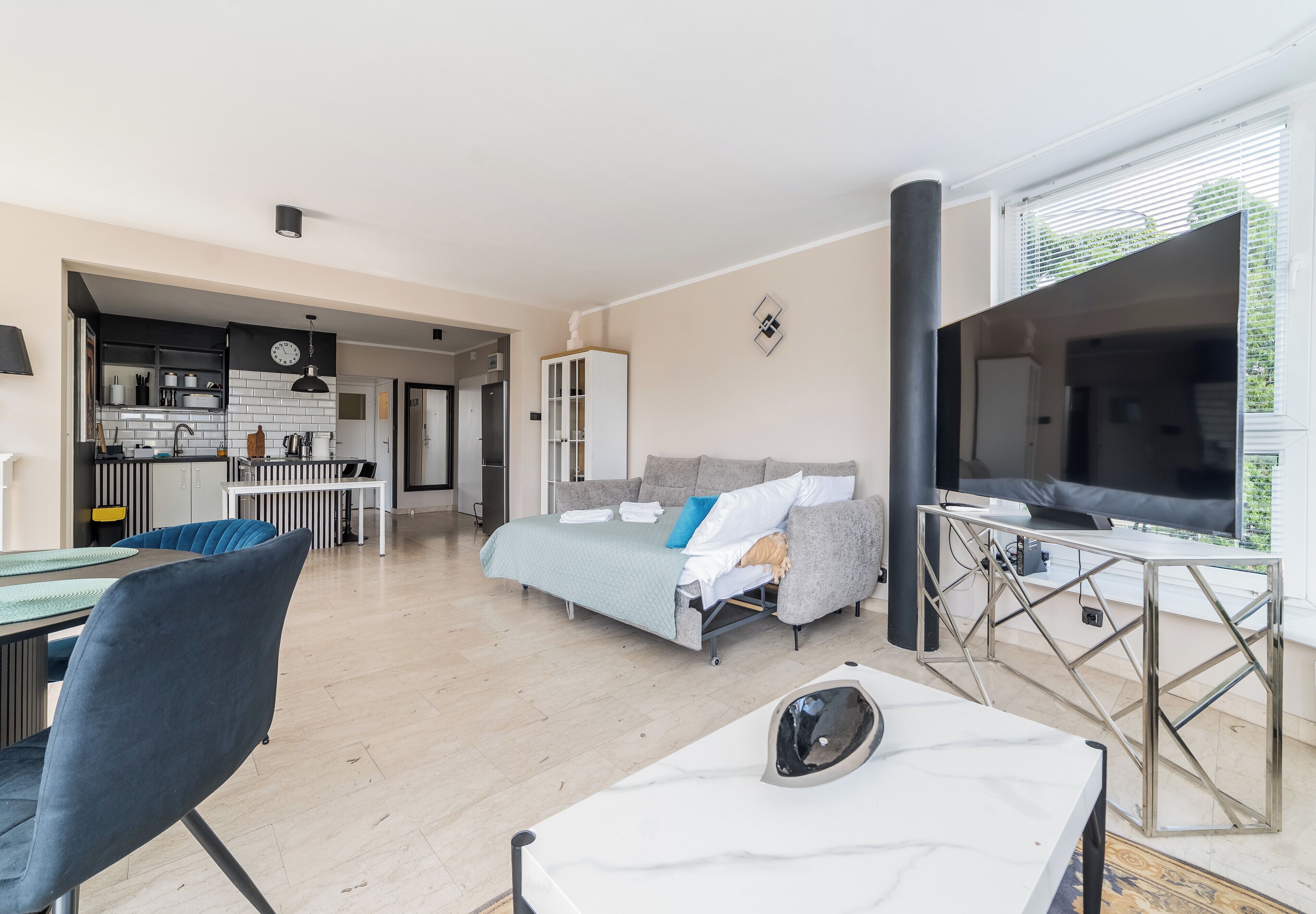 Un espacio habitable moderno con cama, zona de estar, mesa de comedor y una cocina al fondo.