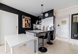 Eine moderne Küche mit einer weißen Kücheninsel, schwarzen Barhocker und einer schwarz-weißen Küchenrückwand.