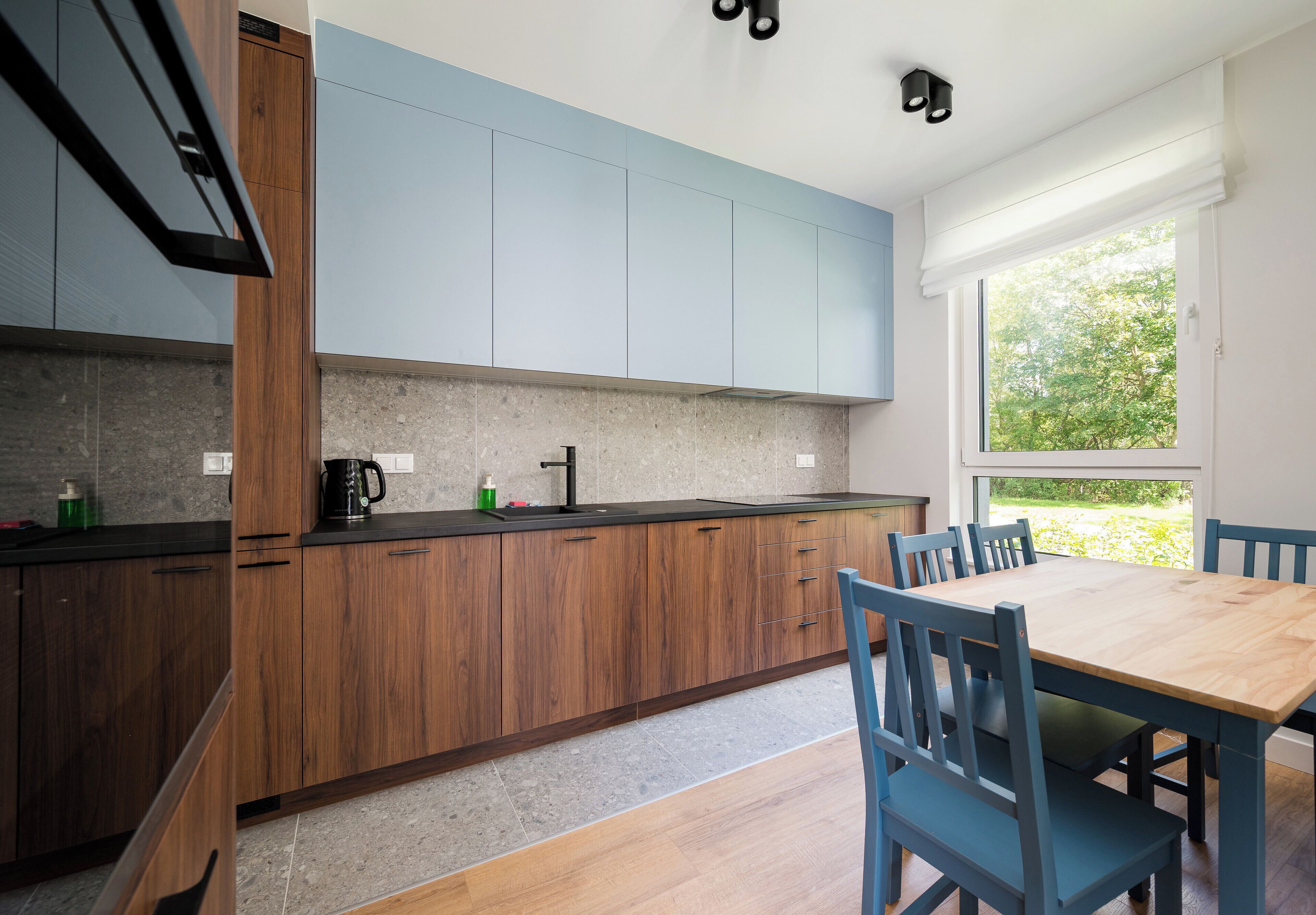 Eine moderne Küche mit Holzschränken, einer schwarzen Arbeitsplatte und einem Essbereich mit Holztisch und blauen Stühlen.