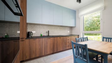 Eine moderne Küche mit Holzschränken, einer schwarzen Arbeitsplatte und einem Essbereich mit Holztisch und blauen Stühlen.
