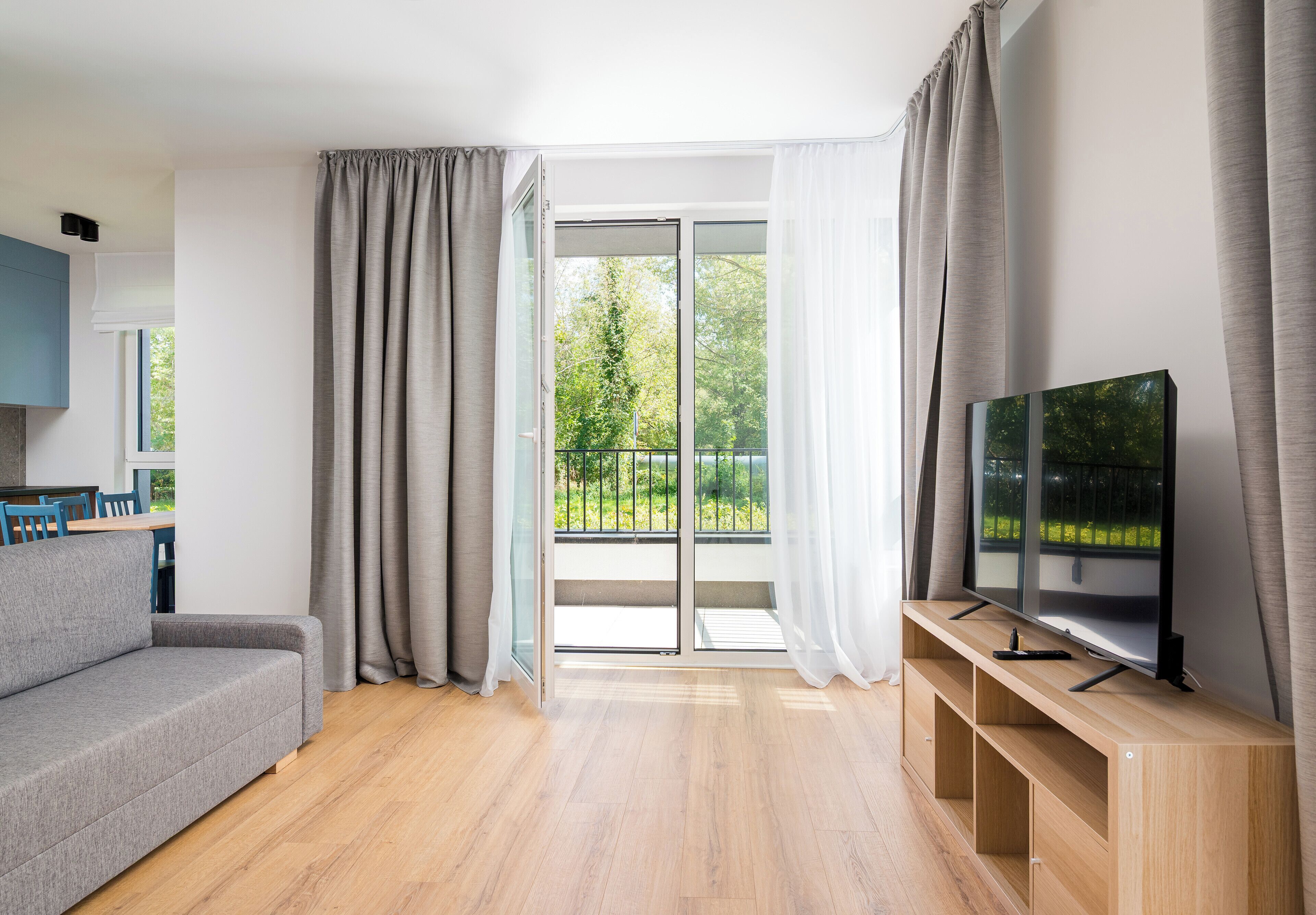 En moderne stue med en grå sofa, et fladskærms-tv på et træstel og en skydedør, der fører ud til en balkon.