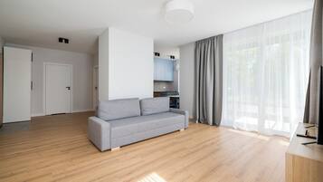 Ein geräumiges Wohnzimmer mit grauem Sofa, Holzböden, einem Essbereich mit Tisch und Stühlen sowie einer Küche mit blauen Schränken.