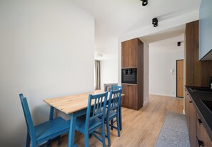 A modern kitchen with wooden cabinets, a built-in oven, and a dining area with a wooden table and blue chairs. - Warszawa Zacisze-Wilno Deluxe Apartment (Warszawa)