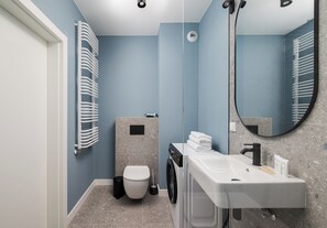 A modern bathroom with a white toilet, a washing machine, a sink, and a mirror. - Warszawa Zacisze-Wilno Deluxe Apartment (Warszawa)