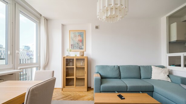 Una sala de estar moderna con un sofá azul, una mesa de centro de madera y un comedor con una mesa y sillas.