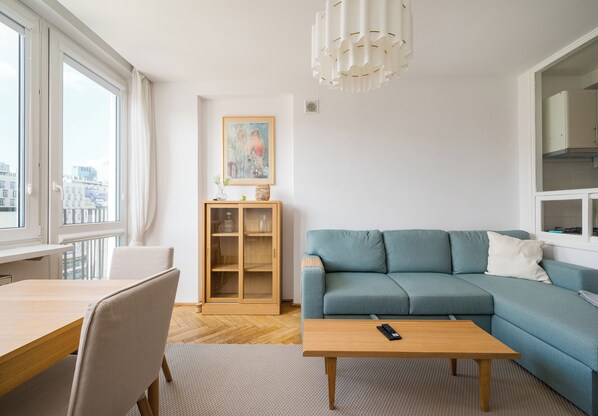 A modern living room with a blue sofa, a wooden coffee table, and a dining area with a table and chairs. - Marszałkowska City View Apartment (Warszawa)