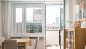 Una sala de estar moderna con comedor, puerta de vidrio que da a un balcón y vistas de edificios de la ciudad.
