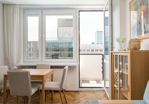 A modern living room with a dining area, a glass door leading to a balcony, and a view of city buildings. - Marszałkowska City View Apartment (Warszawa)