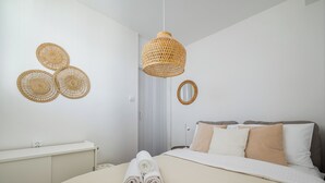 Un dormitorio ordenado con cama, lámpara colgante y espejo adosado a la pared.