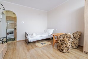 A small, compact room with a bed, a table, two patterned chairs, and a kitchenette in the background. - Park Kozielski Comfort Apartment (Gliwice)