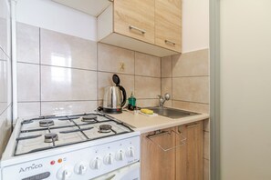 Una cocina con estufa a gas blanca, armarios de madera y un lavamanos de acero inoxidable.
