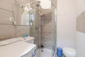 Ett badrum med en dusch som är avskärmad med glasväggar, ett vitt handfat och en toalett.