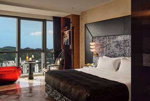 A modern hotel room with a large bed, a red chair, a dining table, and a city view. - Aranciel (Chongqing)