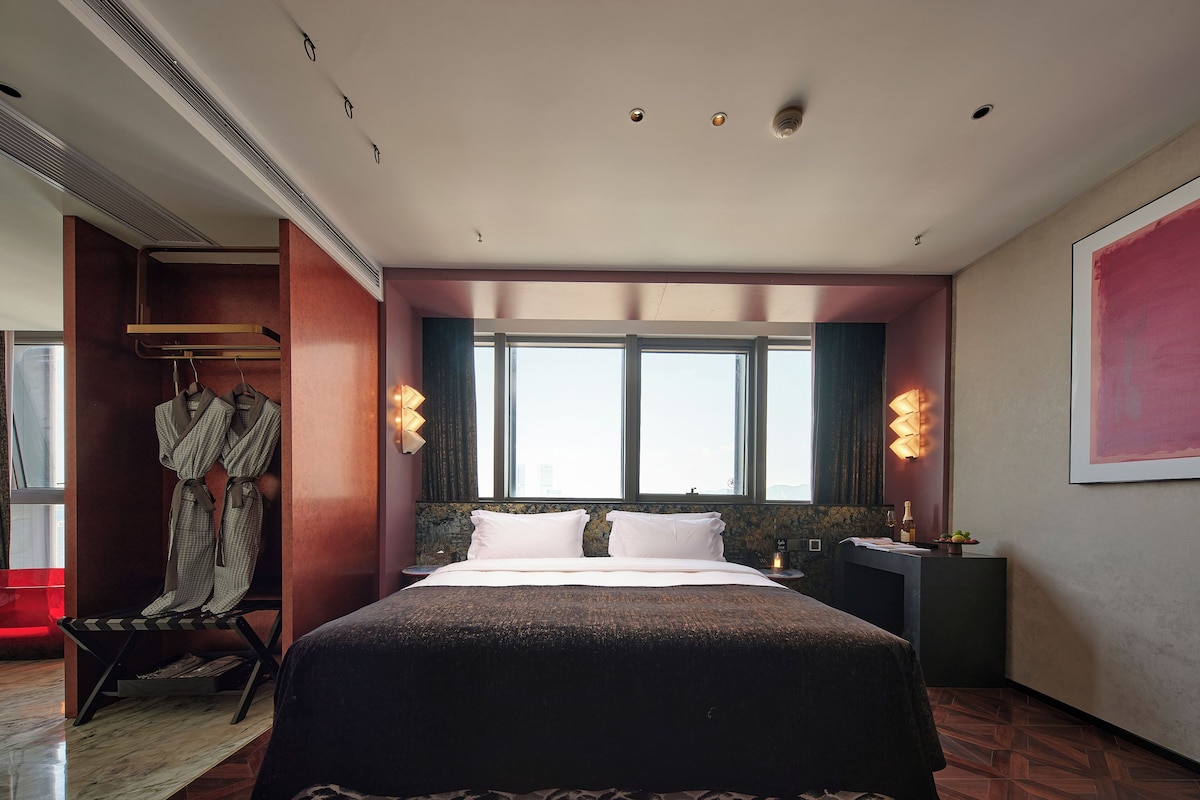 Une chambre d’hôtel avec un grand lit, un porte-peignoir, une table de chevet et une fenêtre avec des rideaux.