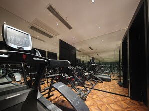 Une salle de sport équipée de matériel d’exercice, dotée d’un mur miroir et d’un plancher en bois à motifs.