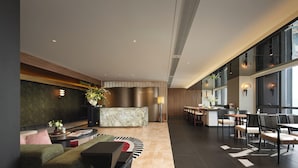 Un hall d’hôtel moderne avec un comptoir d’accueil, un espace salon et de grandes fenêtres.