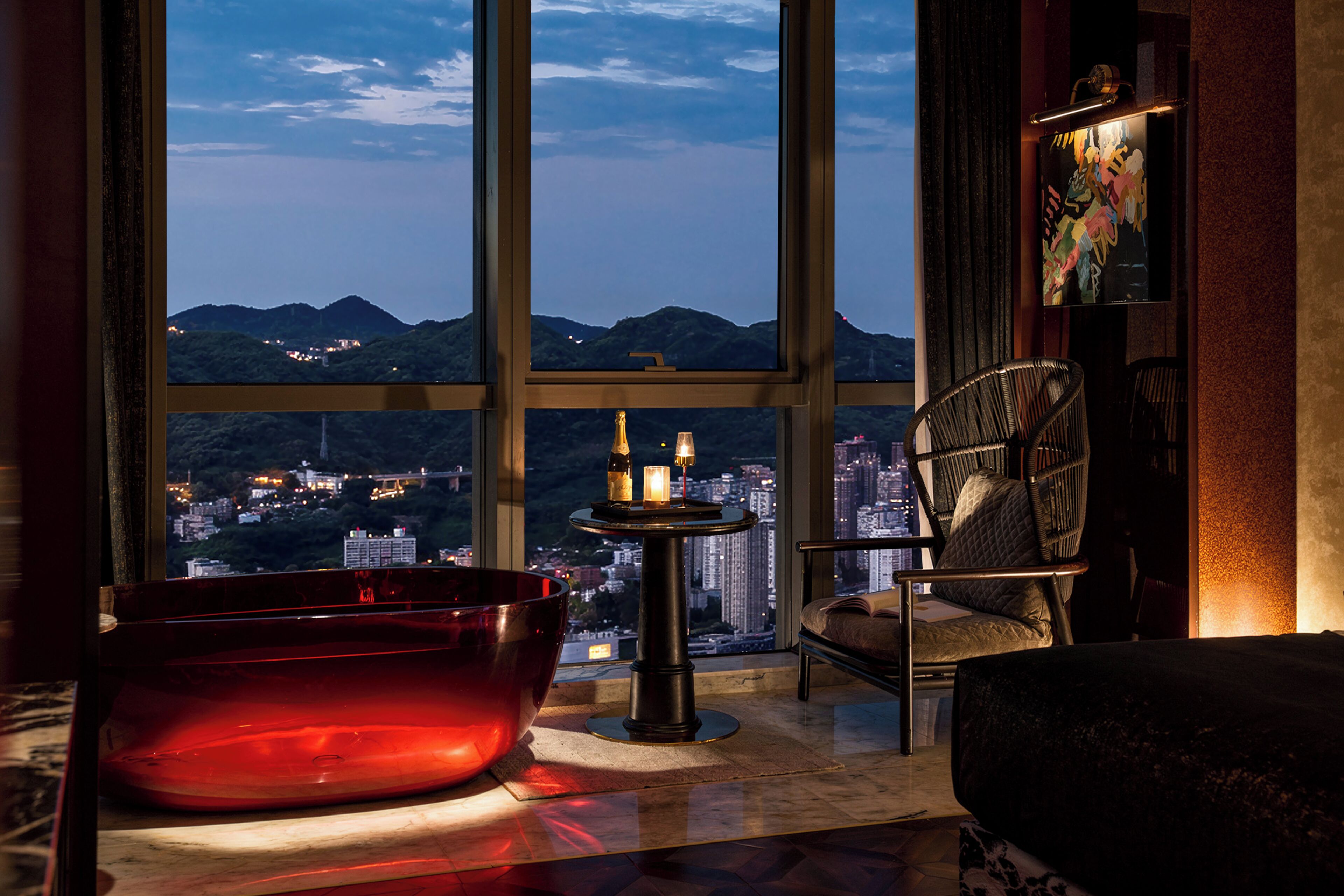 Un intérieur moderne avec une grande fenêtre, une baignoire rouge, une table ronde décorée de bougies et une chaise.