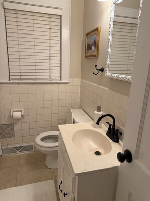 A bathroom with a toilet, sink, and window with blinds. - Charming Historic Bungalow in Emerywood - High Point's Sought-After Neighborhood (High Point)