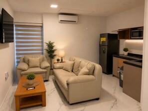 A compact living space with a sofa, a coffee table, a TV, a refrigerator, a microwave, and a small kitchen area. - Enjoyable 1-bedroom apartment with AC in lovely Oranjestad (Oranjestad)