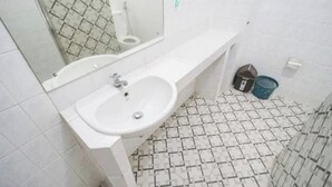 Casa de banho com lavatório branco, espelho e chão em azulejo.