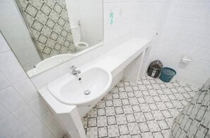 Un baño con un lavabo blanco, espejo y suelo de baldosas.