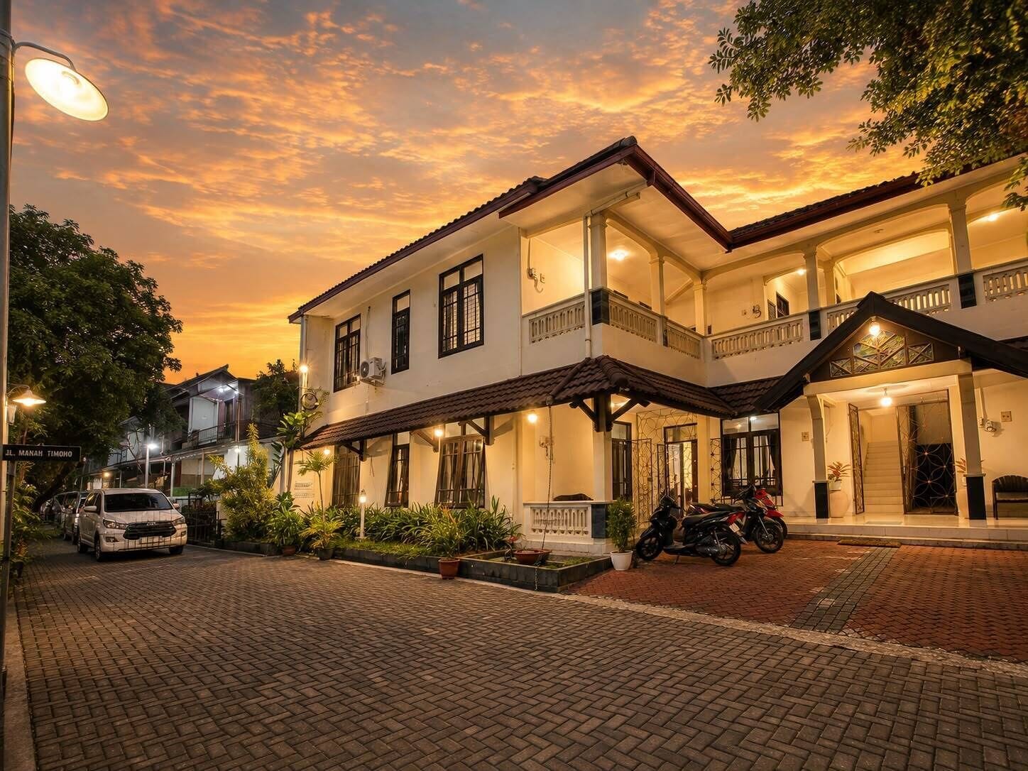 A two-story building with a balcony, a car parked in front, and a motorcycle inside.