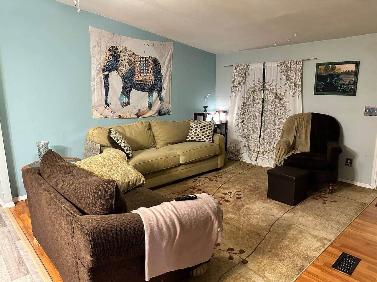 Uma sala de estar com um sofá, uma poltrona, um tapete e um tapeçaria na parede.