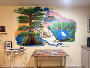 A wall mural with a tree, river, and bird, and a table with a rustic design.