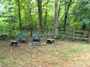 A forested area with outdoor seating including two Adirondack chairs and a small table.