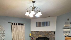 A dining area with a large table, four striped chairs, a chandelier, a stone fireplace, and a wall with motivational signs.